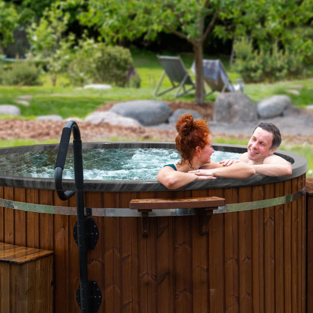 A round wood fired hot tub with marble colors in a garden setting two people looking at each other happy, smiling