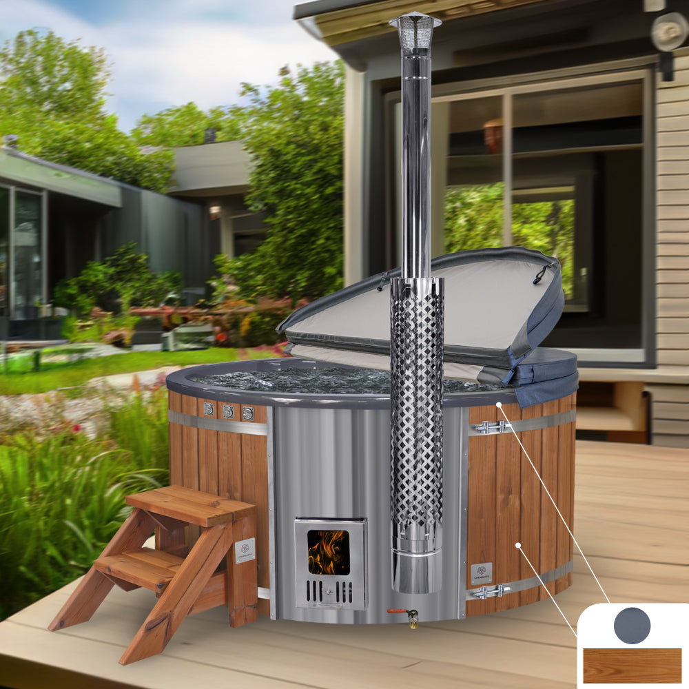 Wood fired hot tub with a grey fiberglass insert, ThermoWood cladding, integrated heater, and chimney, set on a patio with a house in the background.