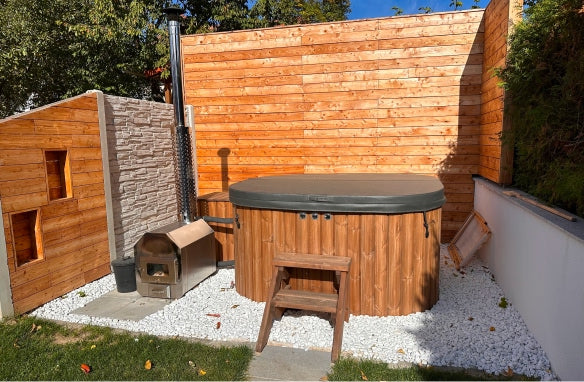 A square-shaped hot tub covered with a lid on the terrace, featuring a filter box, standard steps, and an outdoor stove with a chimney