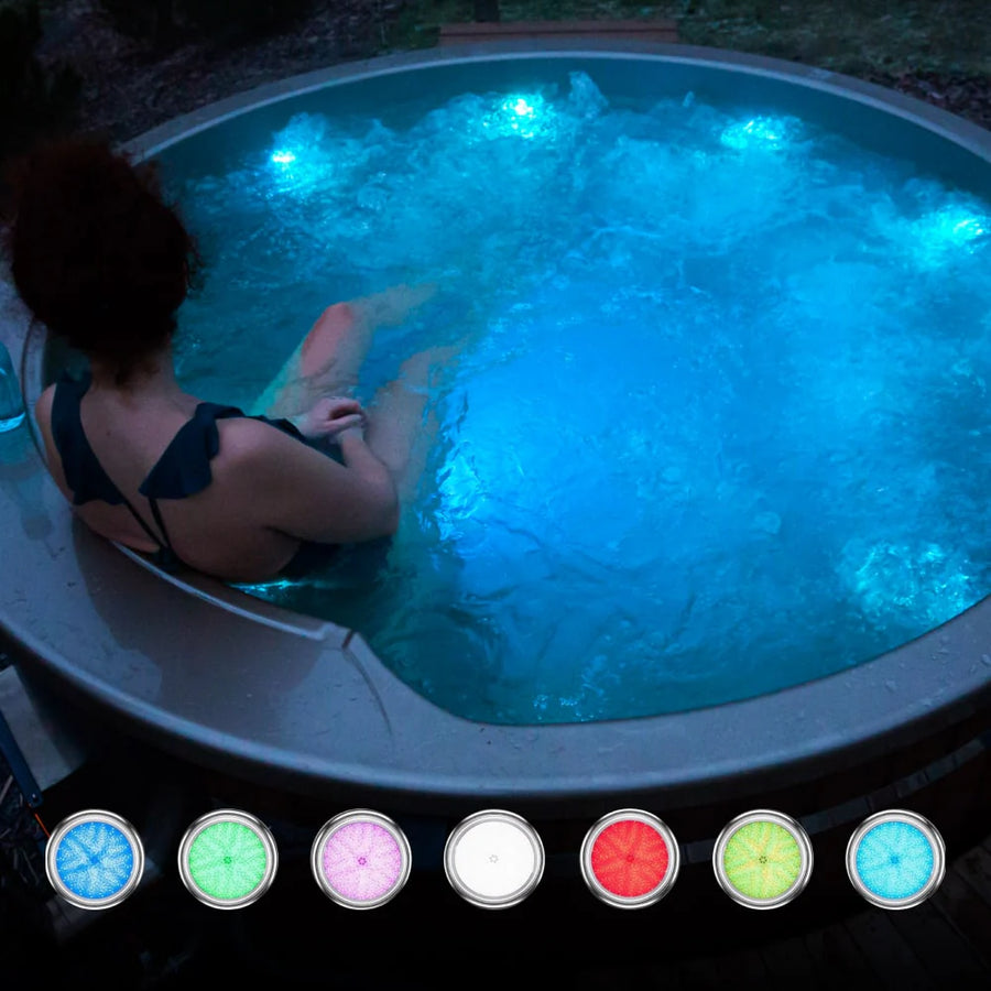 Vue en soirée d'une personne se relaxant dans un bain rond illuminé, de type bain nordique, avec des lumières LED bleues et de l'eau bouillonnante.