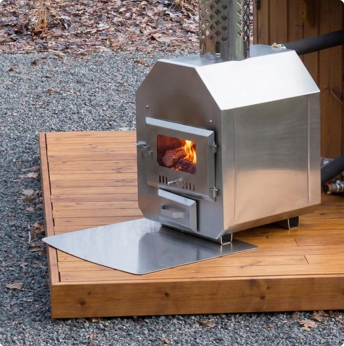 Poêle à bois extérieur en acier inoxydable, posé sur une plaque à cendres, avec un feu qui brûle à l'intérieur.