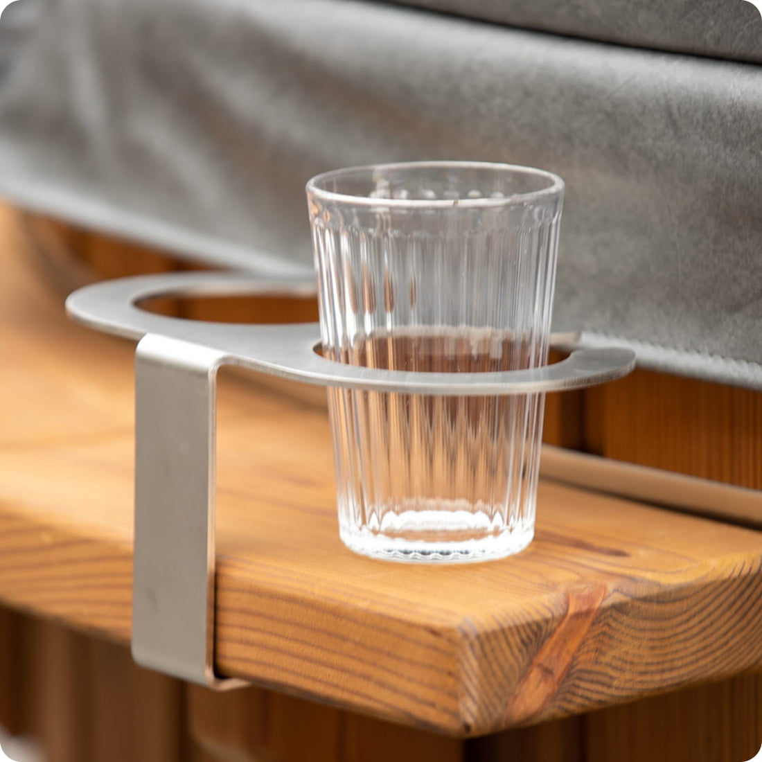 Verre transparent posé sur un support métallique fixé sur une surface en bois avec un couvercle gris en arrière-plan.