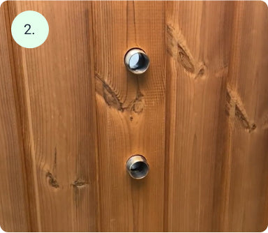 Close-up of two circular metal vents installed vertically on a natural wooden panel surface with visible grain patterns
