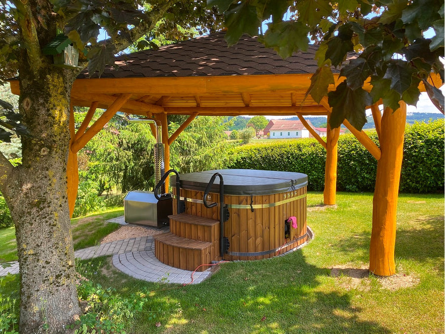 Outdoor view of wooden hot tub with steps and cover under a gazebo surrounded by lush greenery and trees
