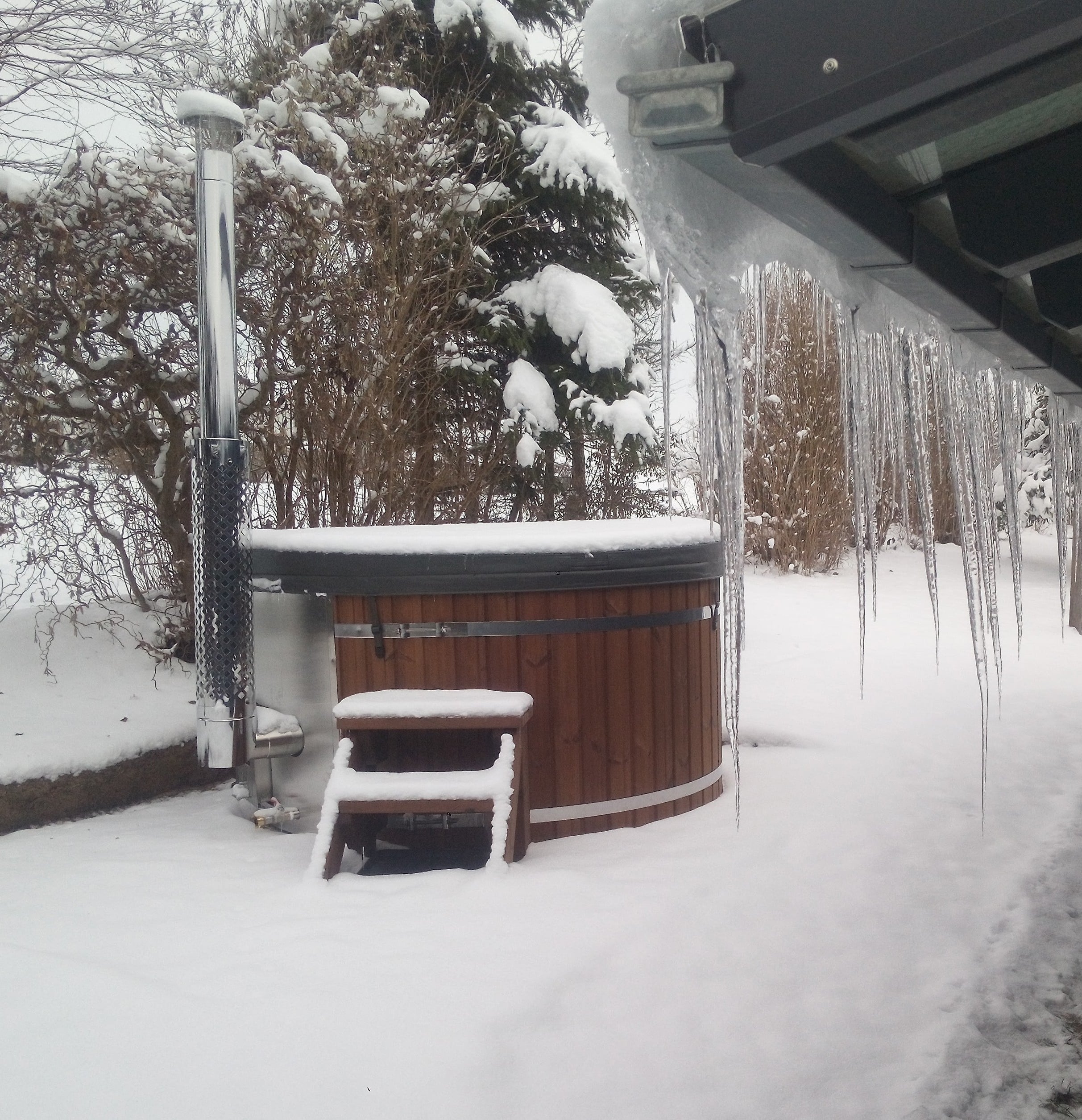 Round wood-fired hot tub covered in snow, demonstrating winter use in freezing outdoor conditions.