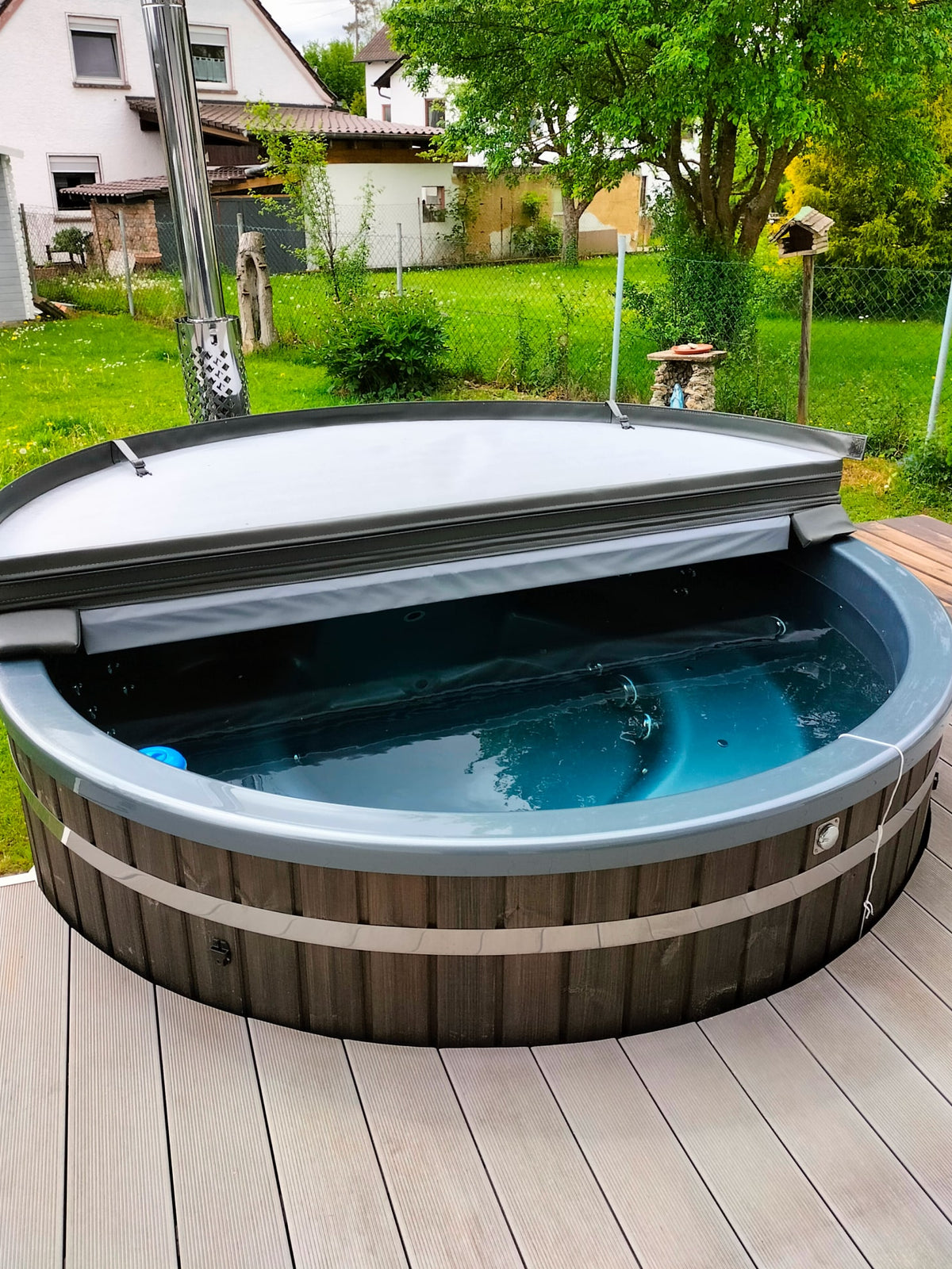 Compact Gardenvity wood fired hot tub with insulated cover in a small green backyard.