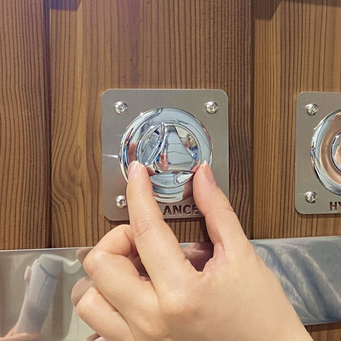 Gros plan sur une main ajustant le bouton de commande chromé portant l'inscription « Drainage » sur un panneau en bois avec garniture métallique en dessous
