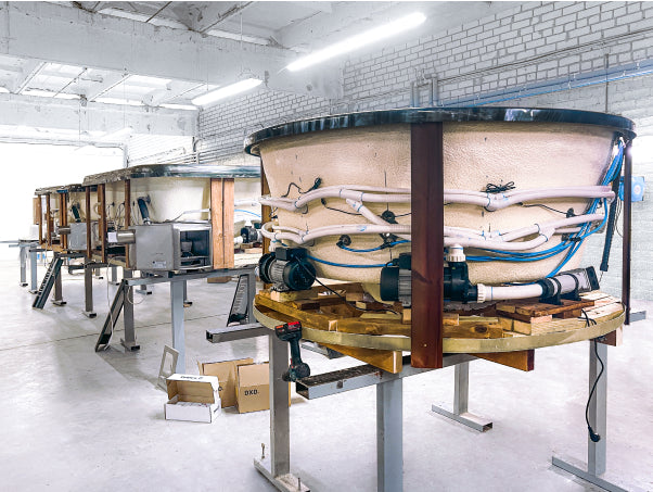 Ligne de production bain nordique chauffée au bois montrant les coques isolées, la plomberie et l'assemblage dans une usine de fabrication européenne