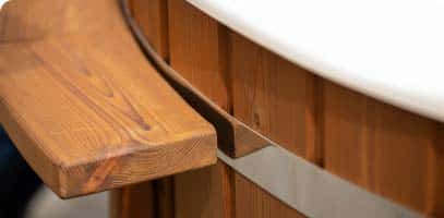Gros plan sur un banc en bois fixé sur le côté d'un bain nordique rond en bois avec une bande métallique et un rebord blanc sur le dessus.