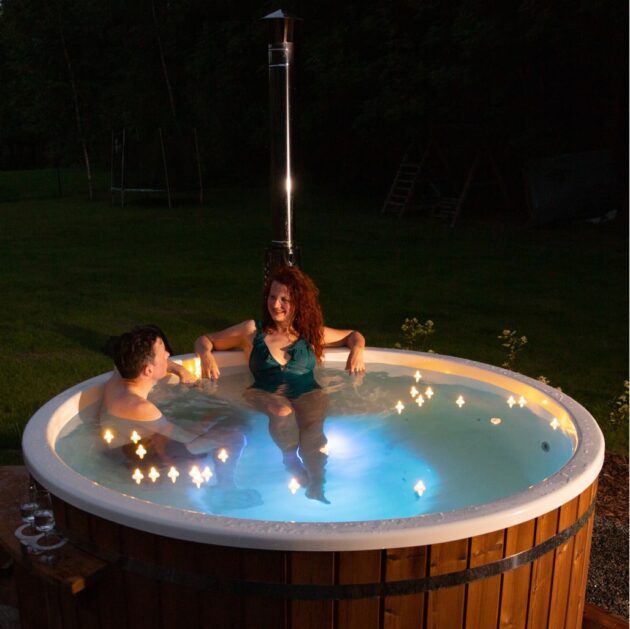 Deux personnes se détendent dans un bain nordique chauffé au bois avec des points de lumière multicolores la nuit